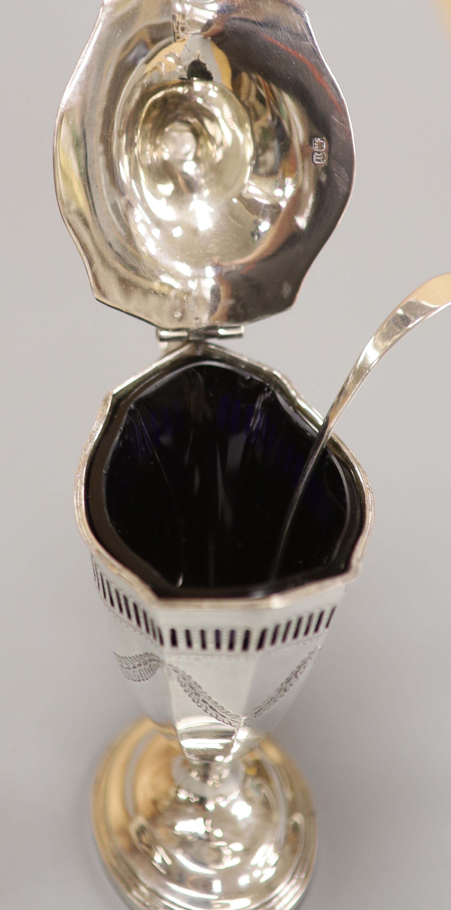 A late Victorian pierced and engraved silver vase shaped pedestal mustard, Nathan & Hayes, Birmingham, 1894, with blue glass liner and an earlier Georgian mustard ladle, height 13.2cm, 147 grams.